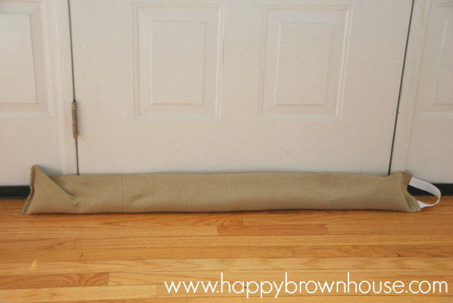 tan tube DIY Door Draft Stopper or draft snake sitting at the bottom of a white door to cover up any cold air drafts