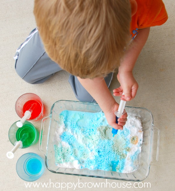 overheard shot of a boy squirting colored vinegar into a glass dish filled with baking soda