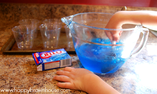 Child\'s hand mixing blue Jello for candy shark jello snack cups