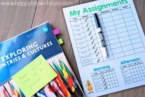 laminated Homeschool Assignment and Chore Chart, dry erase marker, and teacher's curriculum book with sticky tabs attached and sticking out of pages