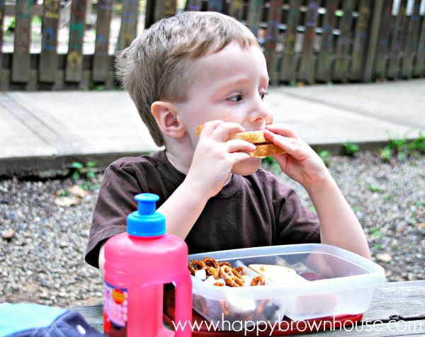 child eating a sandwich during a picnic, red water bottle in the foreground