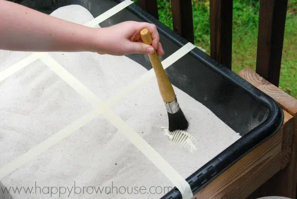 dusting off dinosaur bones in the sand table for archaeologist dramatic play activity