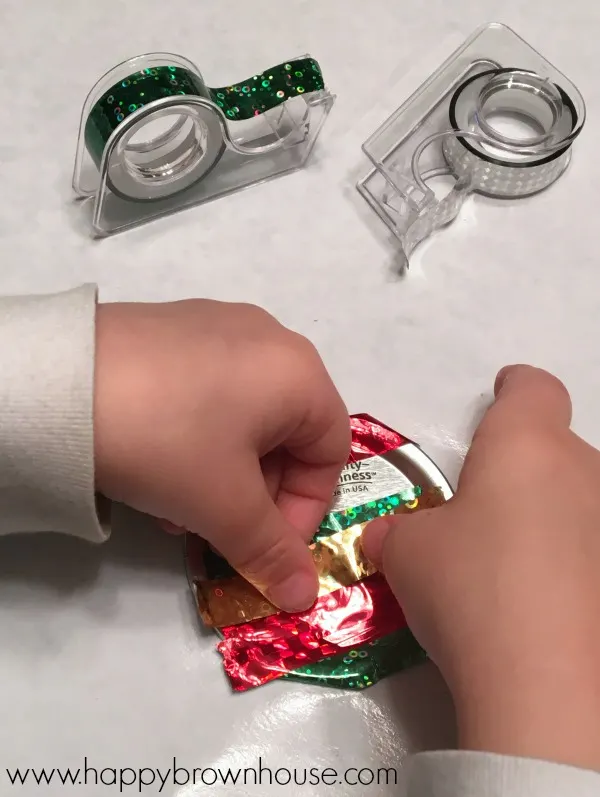 This Kid-Made Washi Tape Mason Jar Lid Ornament is adorable and so simple to make for Christmas. This homemade ornament is perfect for working on fine motor skills. The best part is I already have all the mason jar lids and washi tape for this kids Christmas ornament craft.