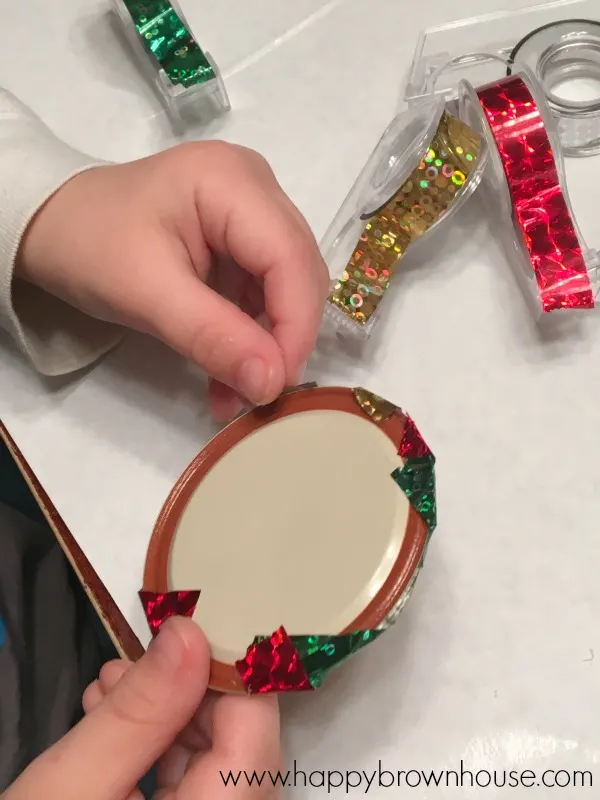 This Kid-Made Washi Tape Mason Jar Lid Ornament is adorable and so simple to make for Christmas. This homemade ornament is perfect for working on fine motor skills. The best part is I already have all the mason jar lids and washi tape for this kids Christmas ornament craft.