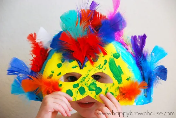 child holding a colorful, feather-filled homemade Rio Carnival Mask in front of their face