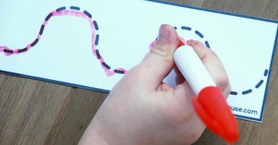 close up of a child\'s hand holding a red dry erase marker while tracing dashed lines for writing practice