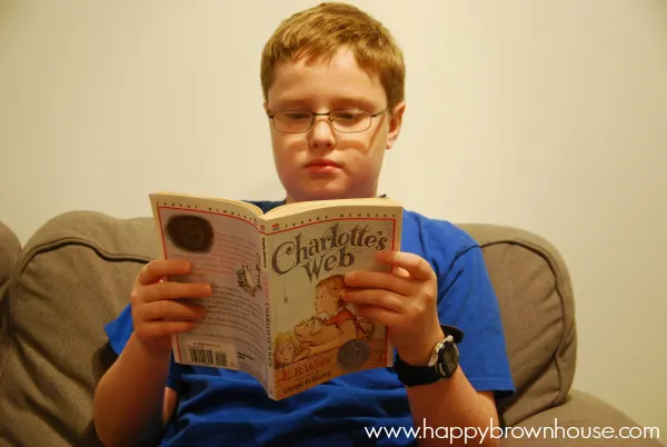 boy in a blue shirt reading Charlotte\'s Web