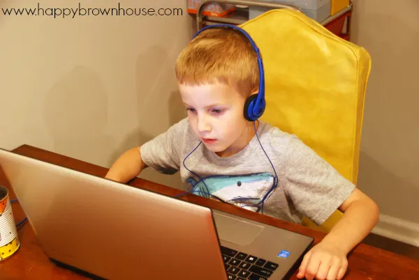 little boy wearing blue headphones and looking at a laptop