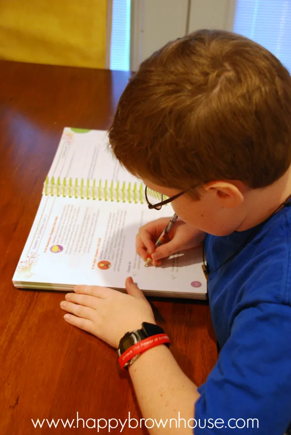 boy in a blue shirt writing in a Readers in Residence homeschool curriculum workbook