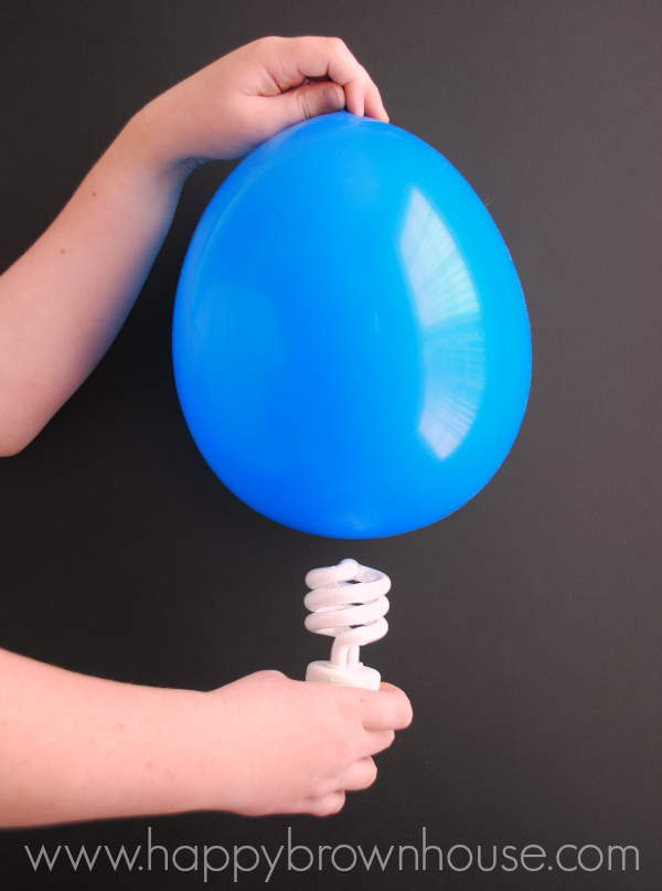 child\'s left hand holding a blue balloon over a light bulb in their right hand, black background