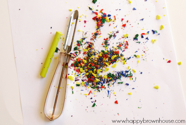 lime green crayon without the paper wrapper metal vegetable peeler and a pile of colorful crayon shavings ready to be used in the Melted Crayon Ornaments