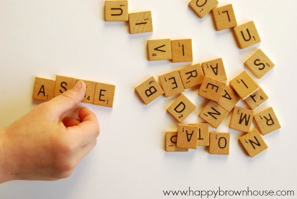 child\'s hand spelling his name with recycled Scrabble Tiles scattered on a white table to make a Scrabble Tile Name Ornament