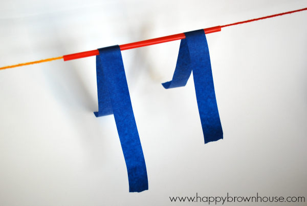 string suspended in air through a red straw, two long strips of blue painter\'s tape attached to the straw in the middle of the tape