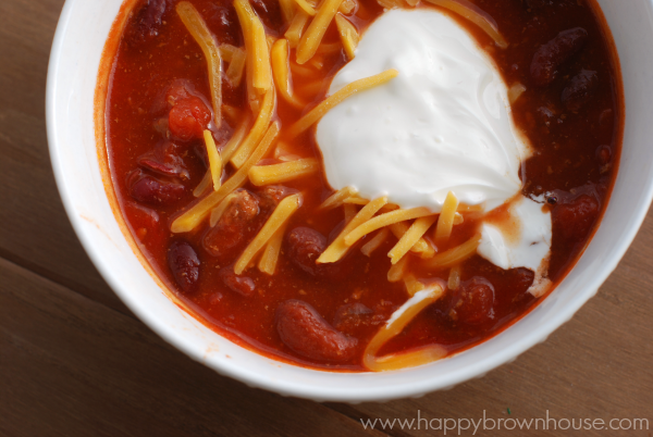 close up of a white bowl of chili full of beans and diced tomatoes topped with cheese and sour cream