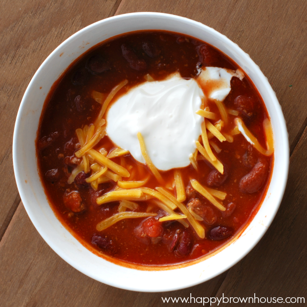 white bowl of chili topped with cheese and sour cream