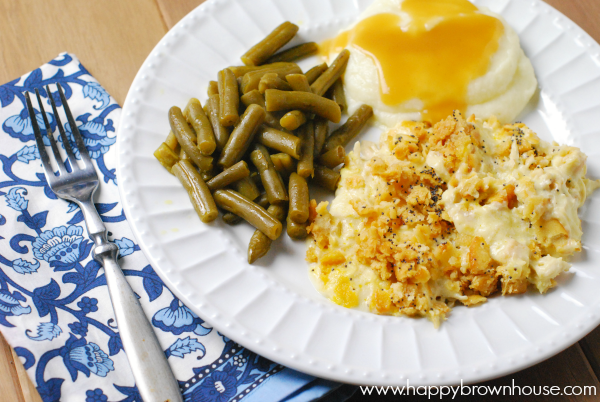 close up of a white plate with Ritz poppy seed chicken casserole, side items, blue napkin, and fork