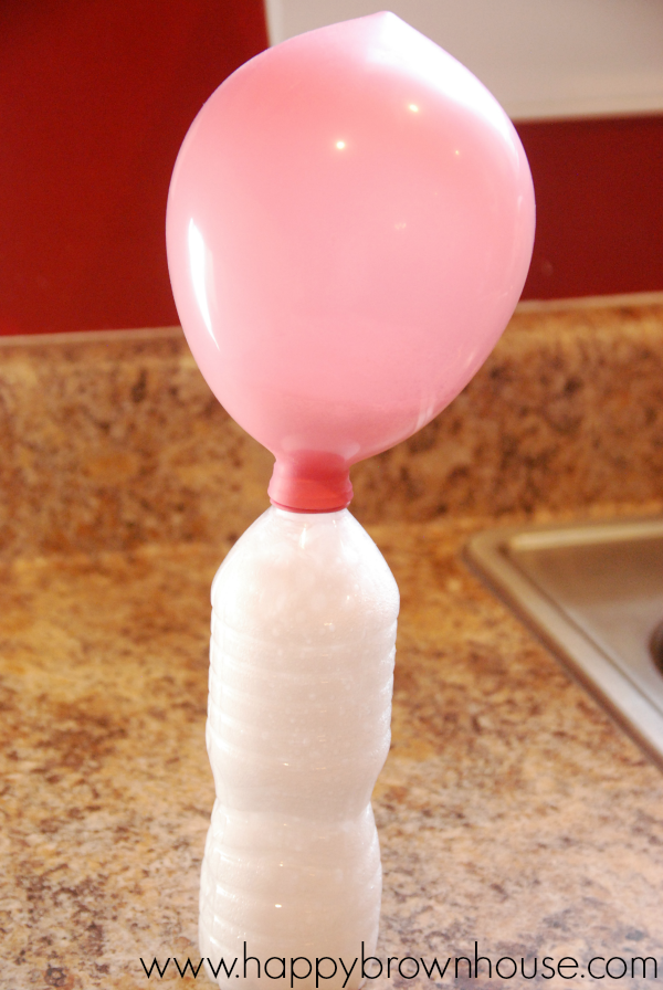 pink balloon attached to a water bottle with white fizz from a chemical reaction during a science experiment