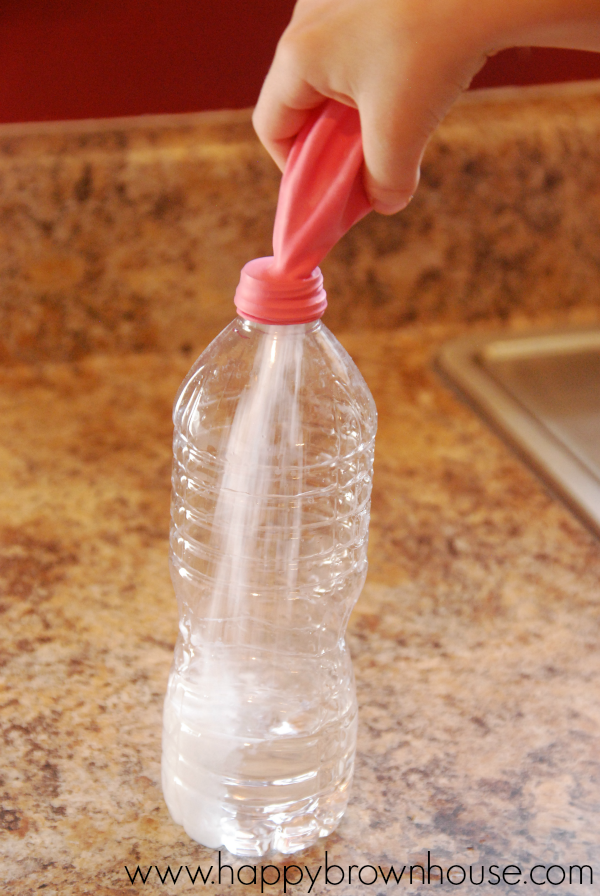 Child\'s hand tipping the pink balloon over and letting the baking soda pour into the vinegar in the water bottle