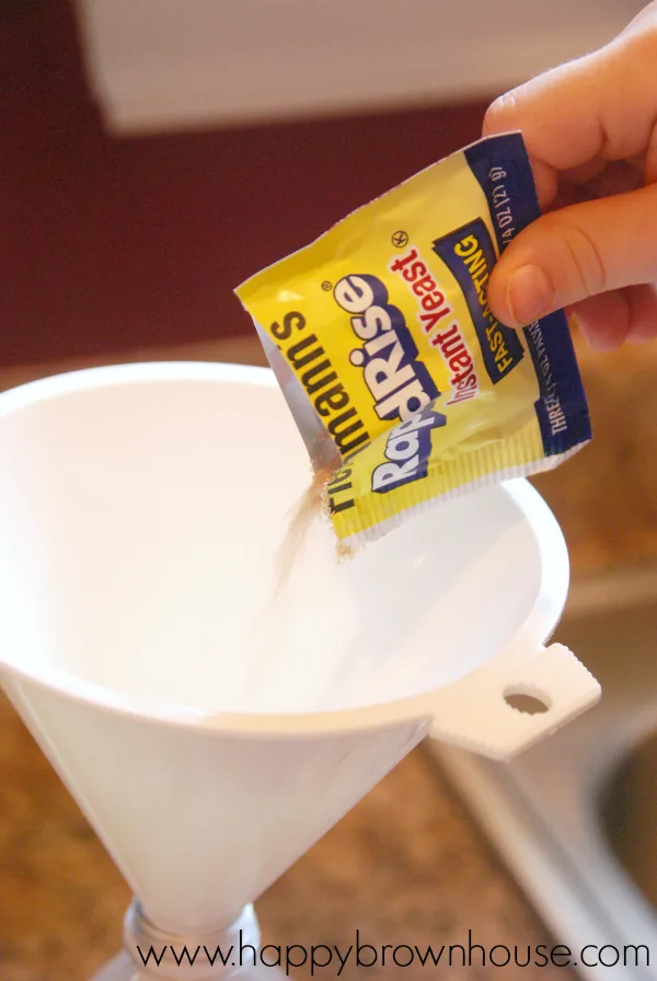 Child\'s hand pouring a yellow packet of instant yeast into a white funnel 