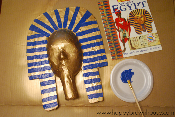 painting blue details on the King Tut mask with the Ancient Egypt craft book for inspiration