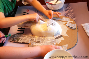 children's hands placing newspaper paper mache pieces on King Tut mask craft