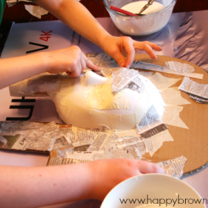 children's hands placing newspaper paper mache pieces on King Tut mask craft