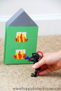 close up of child's hand playing pretend with PLAYMOBIL fire fighter figure and a wooden block house