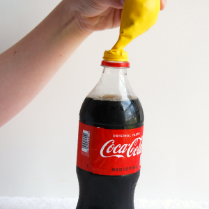 Pouring candy in a yellow balloon into a Coca Cola soda bottle for the Soda and Candy Balloon Science Experiment for kids