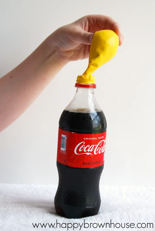 Pouring candy in a yellow balloon into a Coca Cola soda bottle for the Soda and Candy Balloon Science Experiment for kids