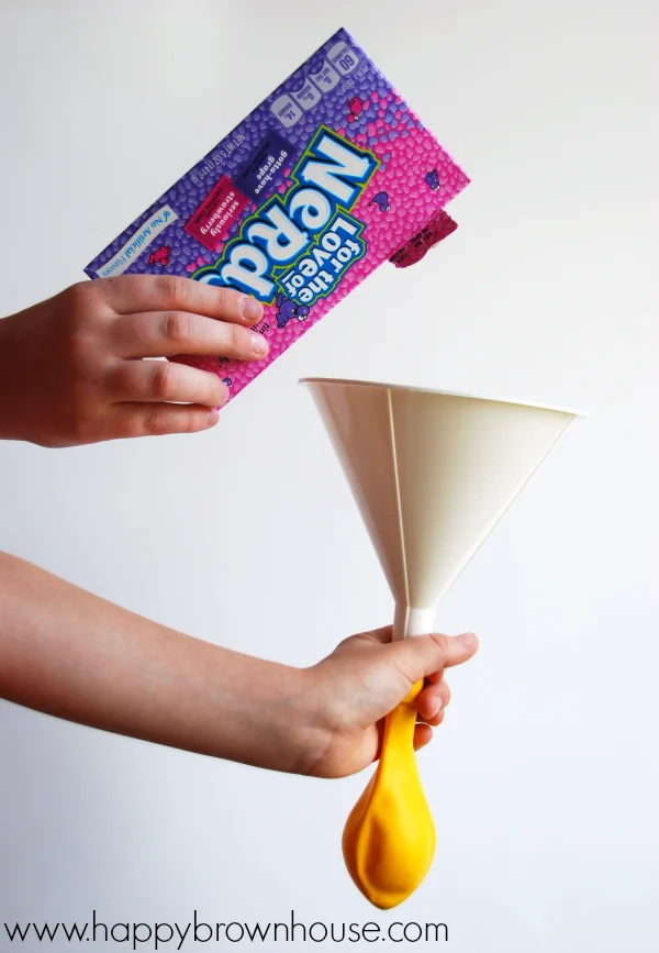 Pouring Nerds candy into a funnel attached to a balloon for the Soda and Candy Balloon Science Experiment