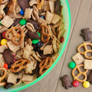 close up of Teddy Bear Trail Mix ingredients in a green bowl with some pieces scattered on the brown background