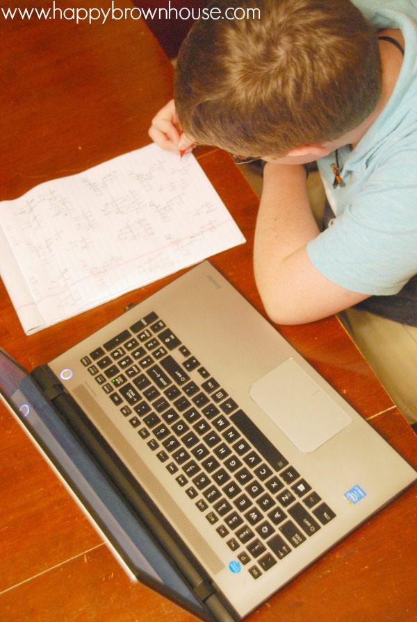 overhead view of child doing math calculations on a piece of paper sitting next to a laptop
