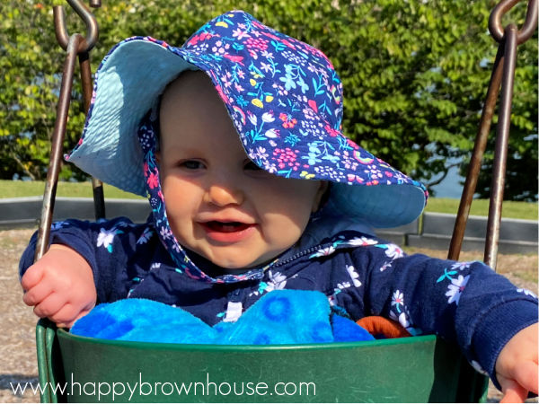 Cute baby with a floppy hat sitting in a baby swing at the park