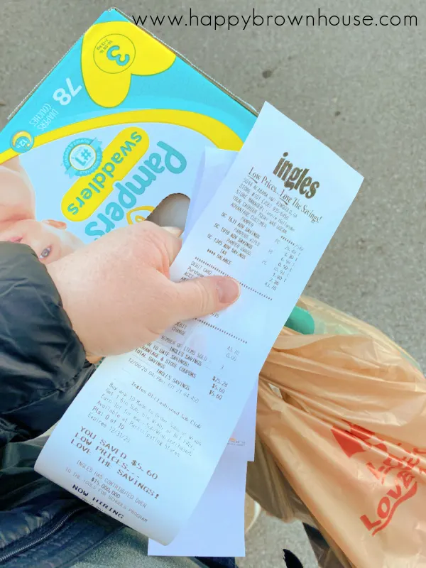 hand carrying grocery bags, diaper box, and Ingles Supermarket receipt