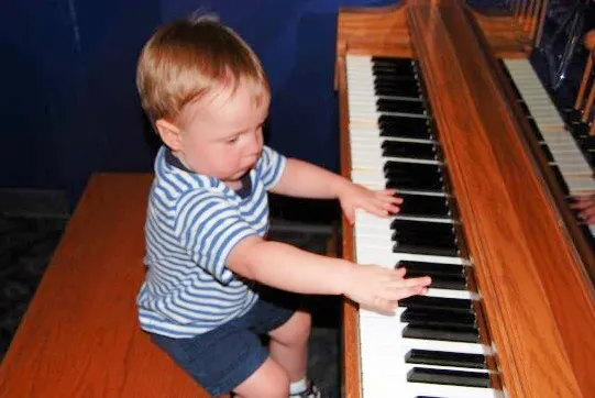 toddler boy in a blue striped shirt playing a piano