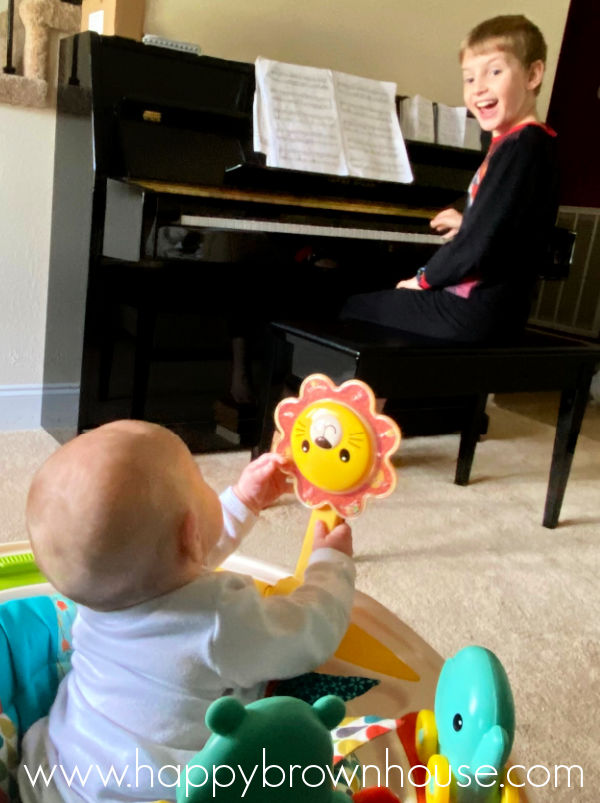 baby sitting in a baby activity seat watching big brother play piano