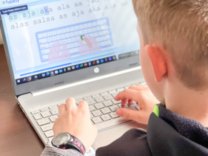 child typing on a computer keyboard with a learning how to type lesson on the screen